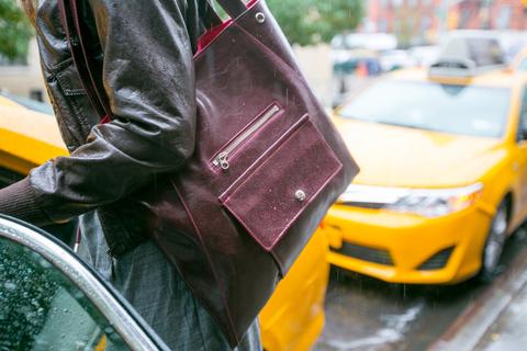 a woman carrying a coated canvas tote bag getting wet in the rain outside a NYC taxicab