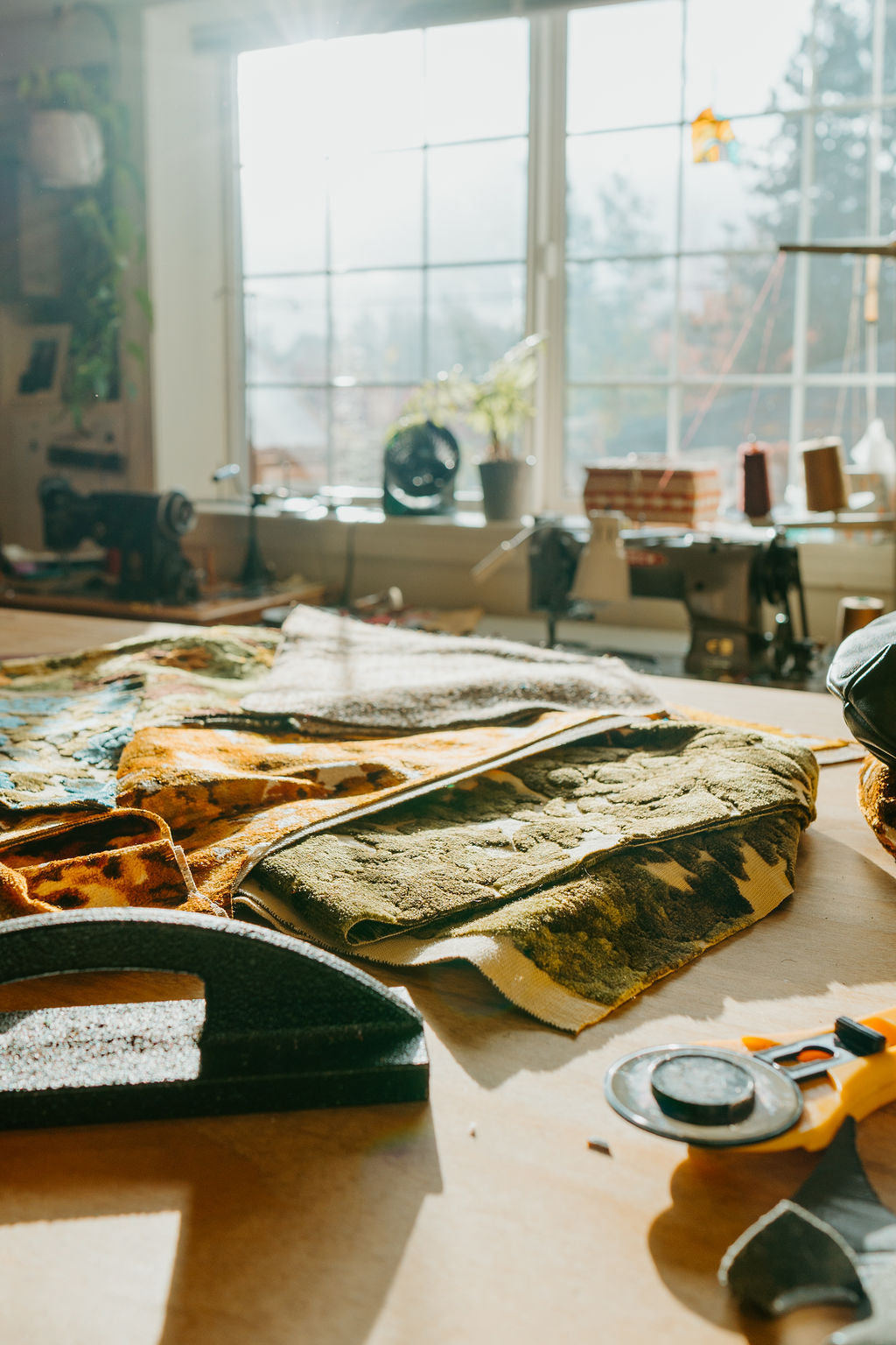 a work table in a handbag shop with sewing tools and fabrics in a sunlit window
