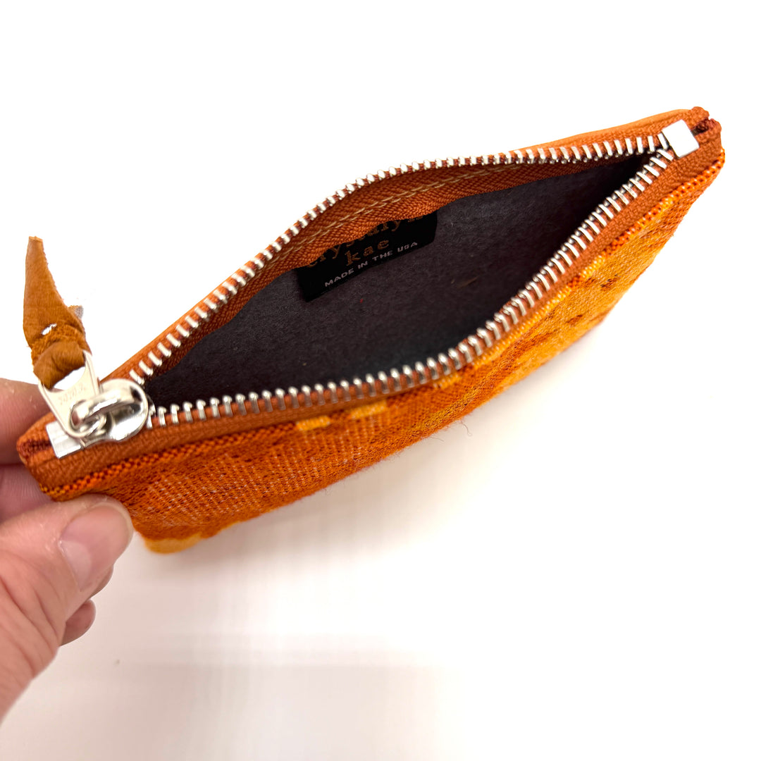 Brown woven pouch with a zipper held by a hand on a white background#color_orange-ferns
