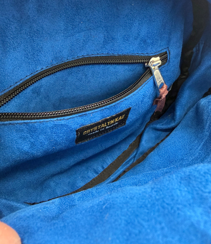 Close-up of a blue purse lining with a brand label on a zipper.#color_black-purple-clouds-airplane-fabric