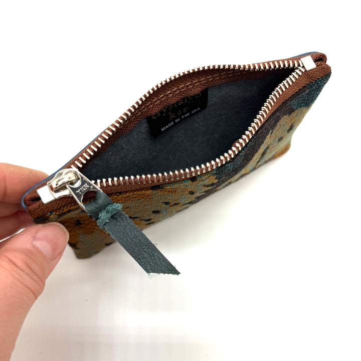 Hand holding a patterned pouch with a zipper, showing the interior.#color_blue-ferns