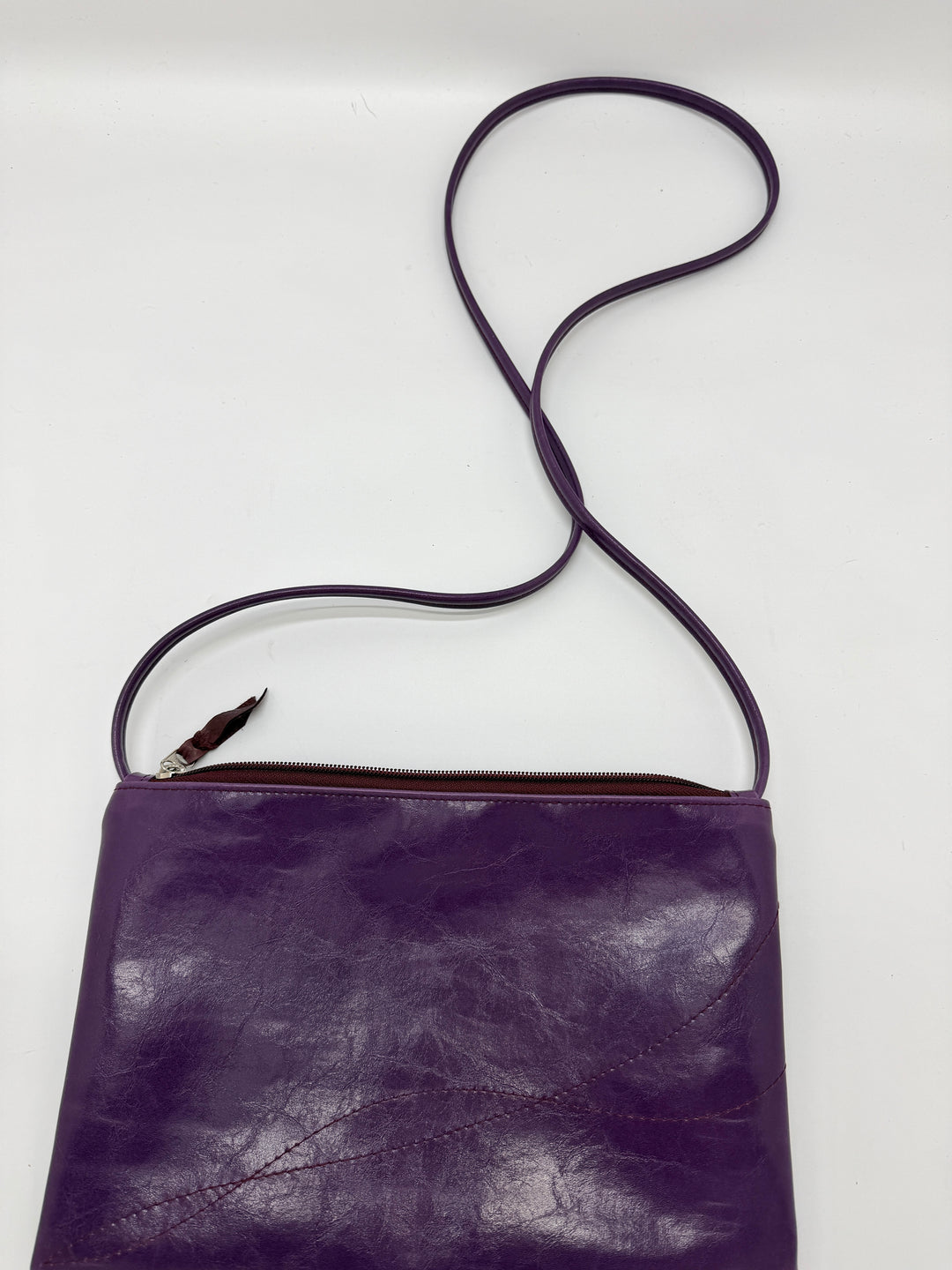Purple leather crossbody bag with a strap on a white background#color_plum