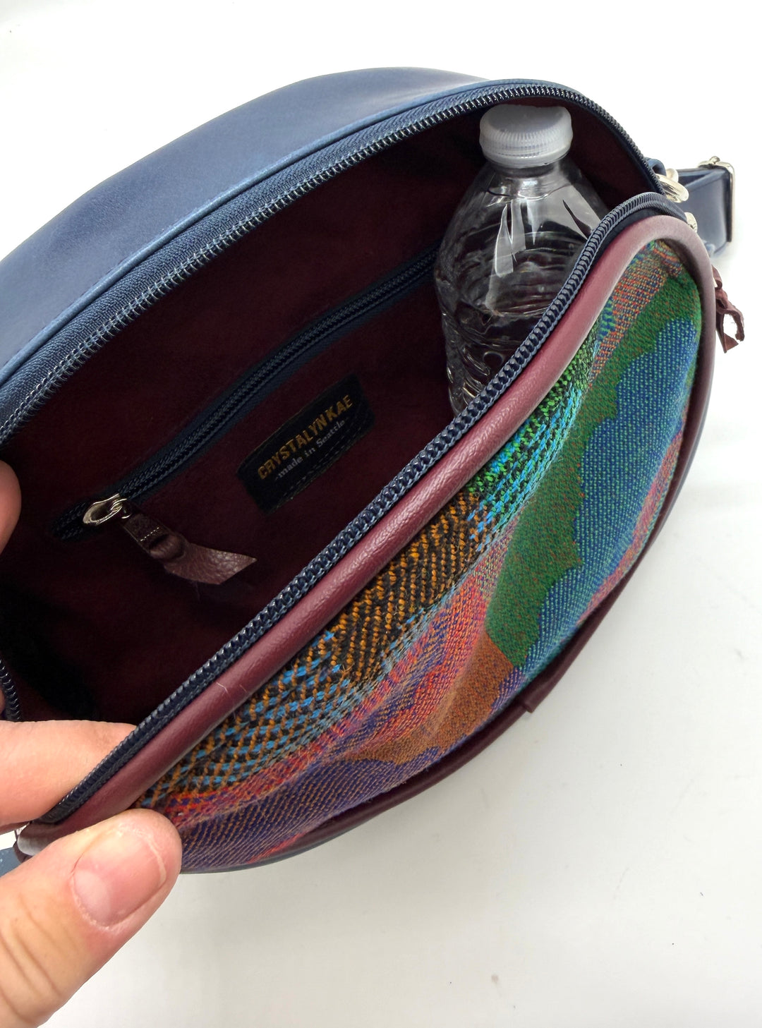 Blue bag with a colorful interior pocket, held open to reveal a water bottle inside.#color_navy-clouds-airplane-fabric