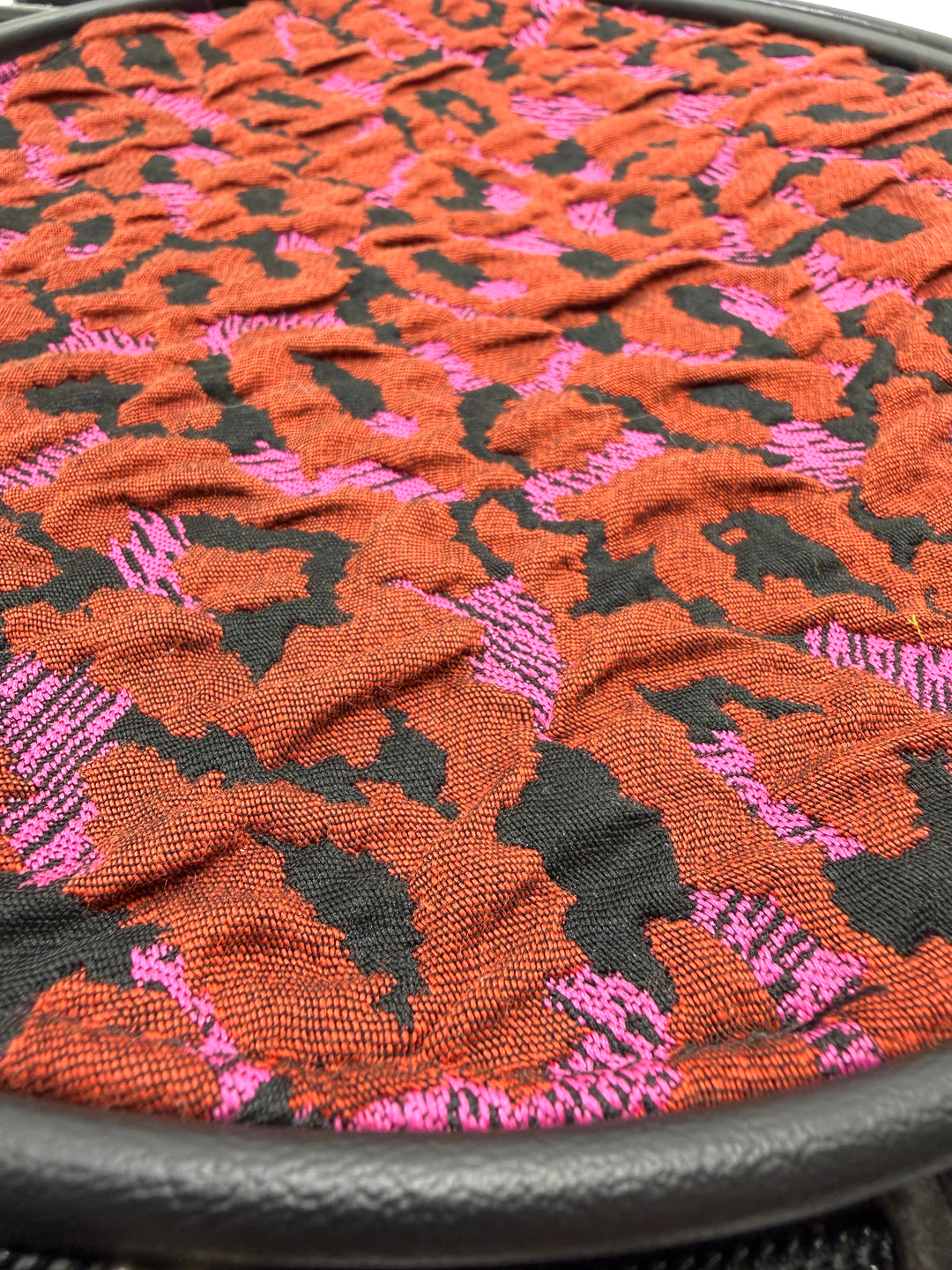 Close-up of a textured fabric with a floral pattern in red, black, and pink on a circle bag#color_poppy-leopard