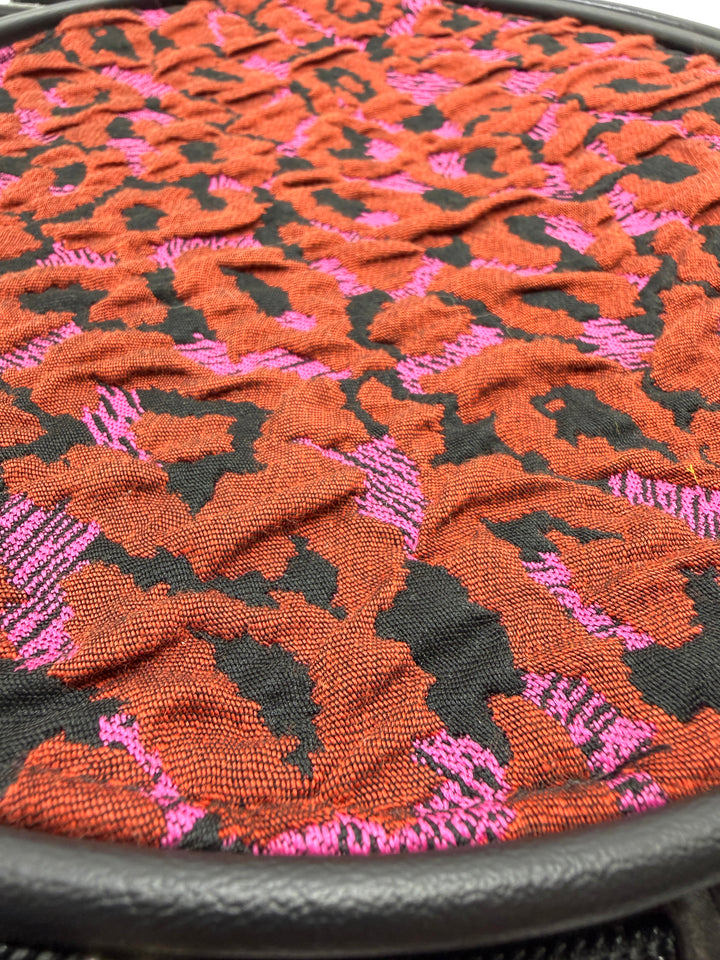 Close-up of a textured fabric with a floral pattern in red, black, and pink on a circle bag#color_poppy-leopard