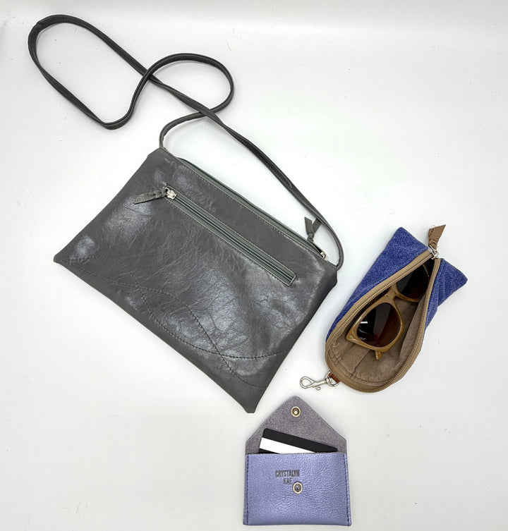Gray leather crossbody bag with a smaller pouch and sunglasses on a white background