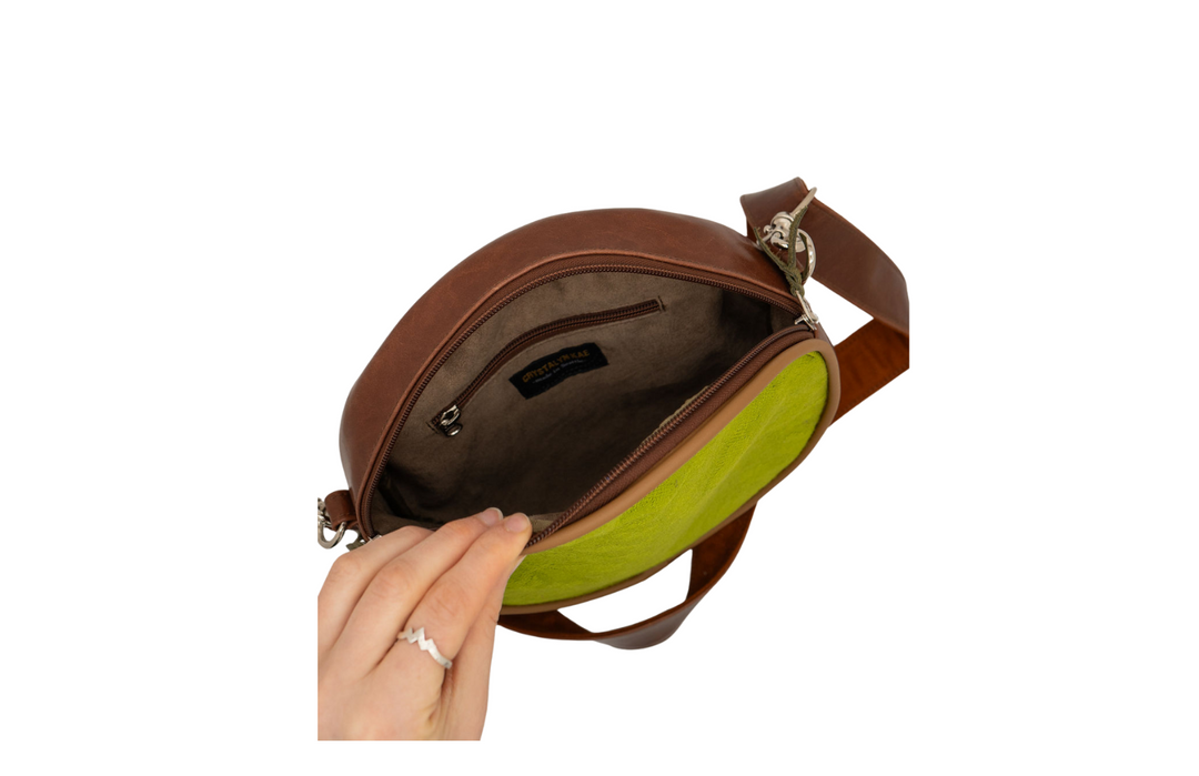 Brown leather crossbody bag with a green interior, held open by a hand on a white background.#color_aerolinas-argentinas-green