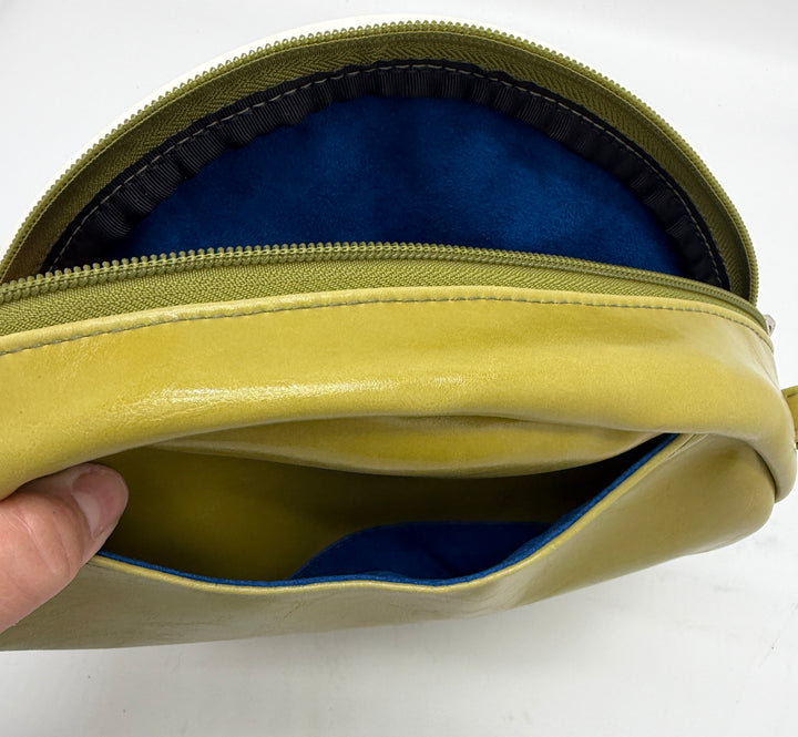 Green leather pouch with blue interior held by a hand on a white background#color_citrine-clouds-airplane-fabric