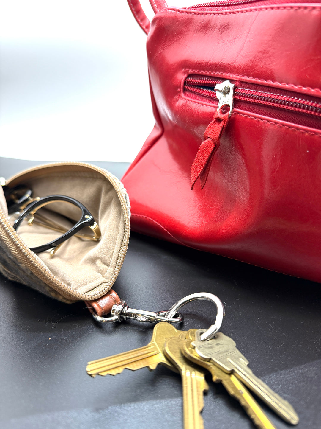 Red handbag with keys and a beige pouch on a dark surface