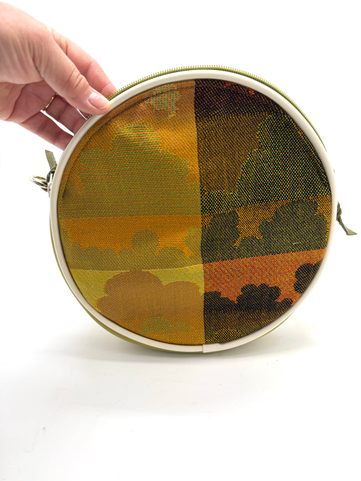 Round pouch with camouflage pattern held by a hand on a white background#color_citrine-clouds-airplane-fabric