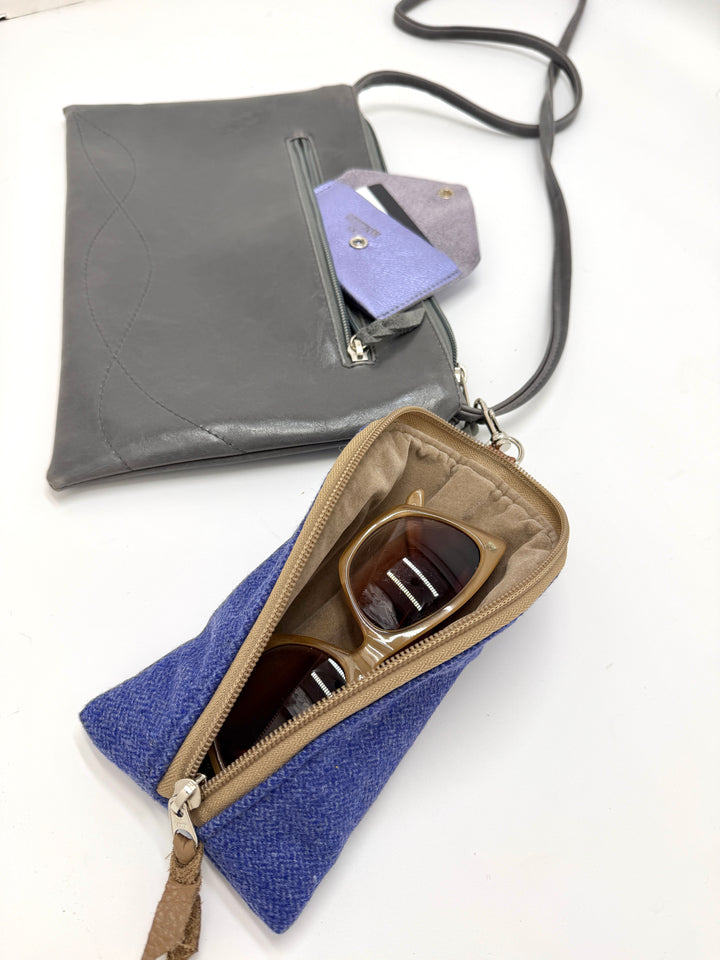 Gray crossbody bag with a blue pouch containing sunglasses on a white background
