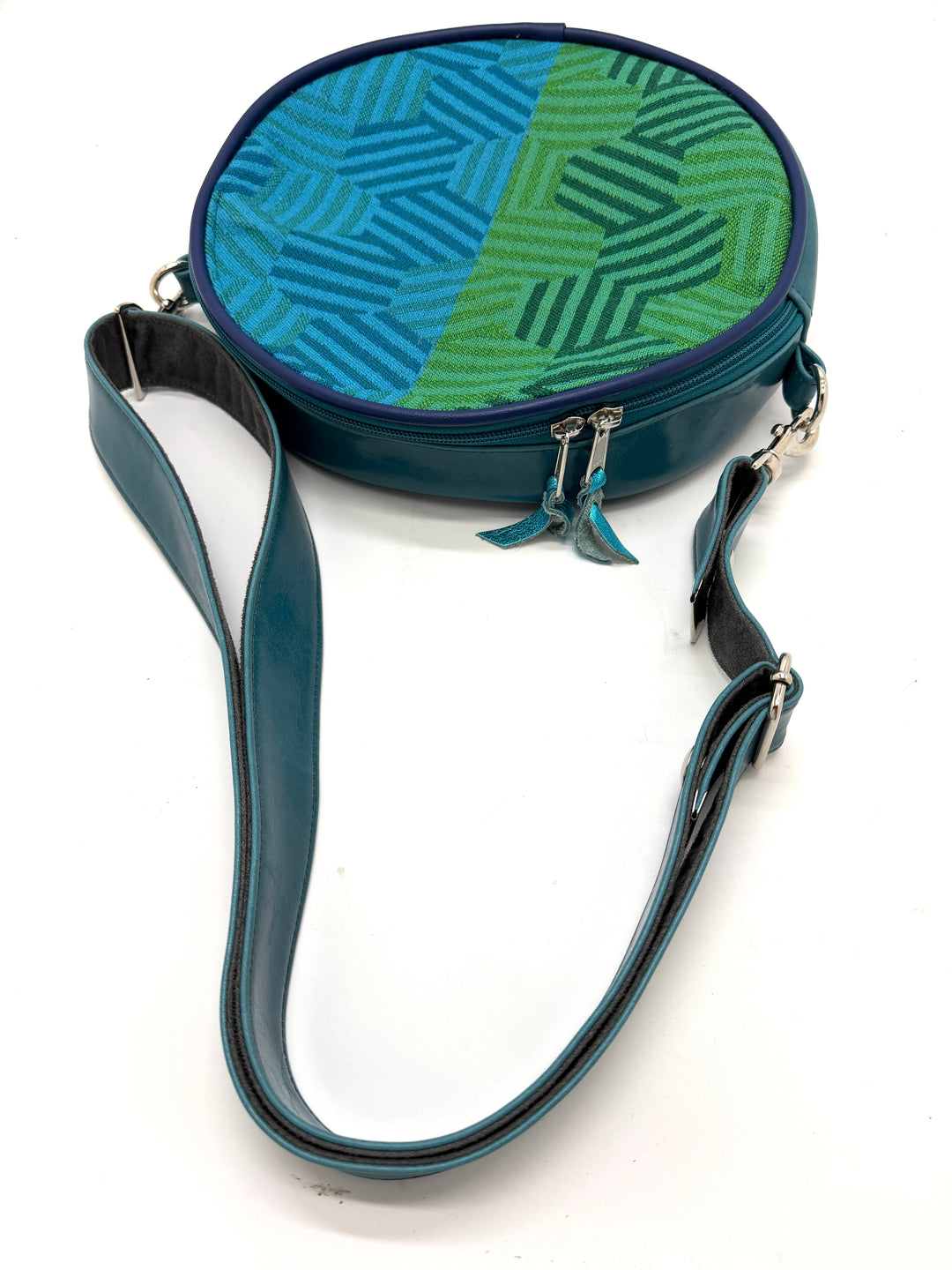 Round crossbody bag with blue and green patterned top and plain bottom on a white background#color_navy-teal-hexagon-airplane-fabric