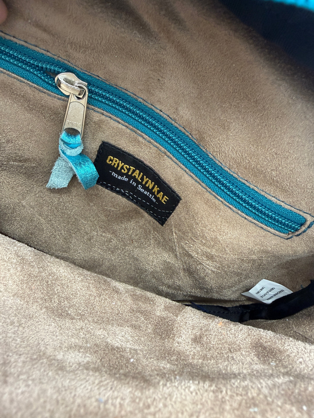 Close-up of a textured fabric with a blue zipper and a brand label on a beige background.#color_navy-teal-hexagon-airplane-fabric