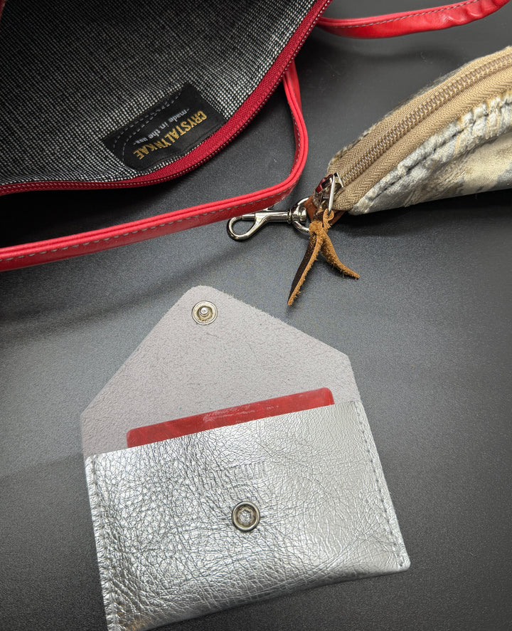 Close-up of a silver leather cardholder with a red interior on a gray surface.
