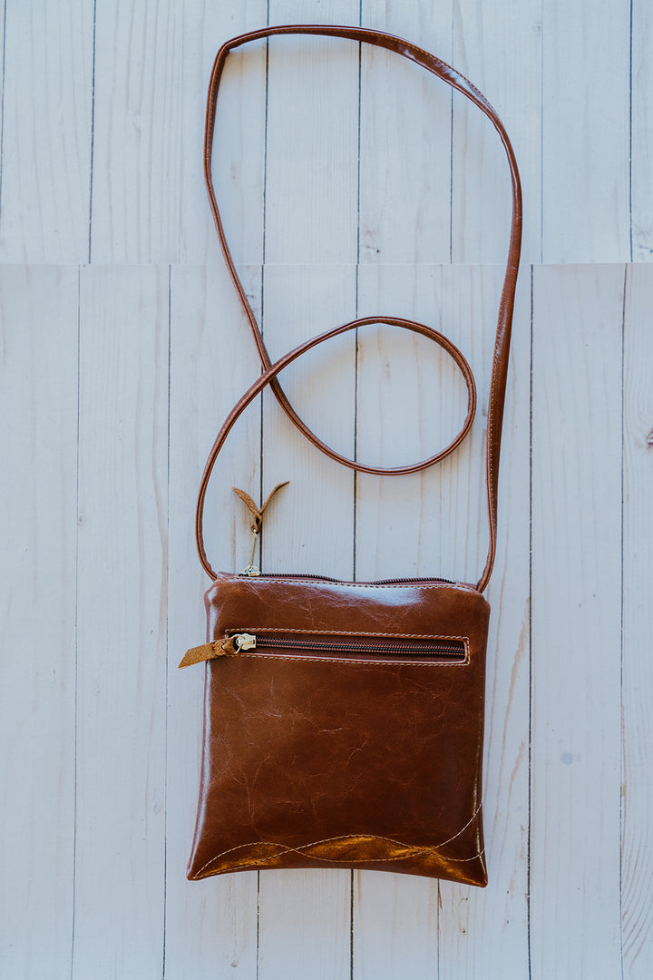 Brown leather crossbody bag on a light wooden surface#color_aerolinas-argentinas-green