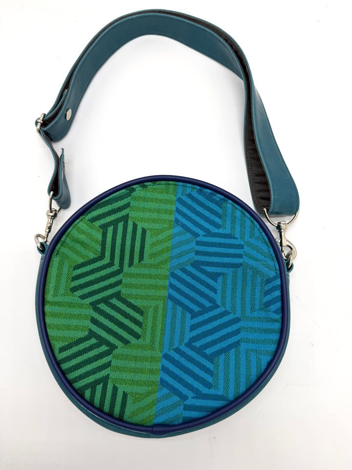 Round crossbody bag with green and blue geometric pattern on a white background#color_navy-teal-hexagon-airplane-fabric