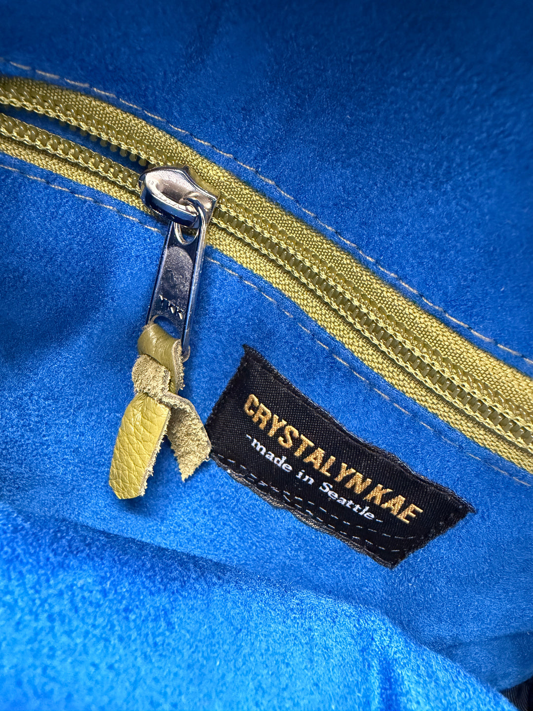 Close-up of a blue fabric with a gold zipper and Crystalyn Kae label.#color_citrine-clouds-airplane-fabric