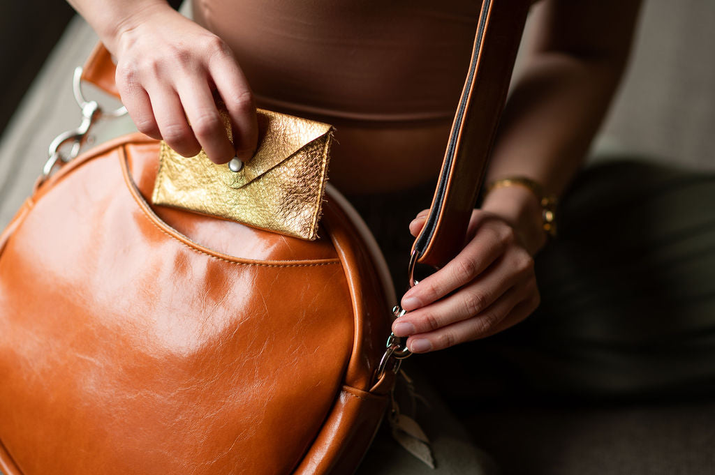 Person holding a brown leather handbag with a gold clutch. #color_white-french-floral-brocade