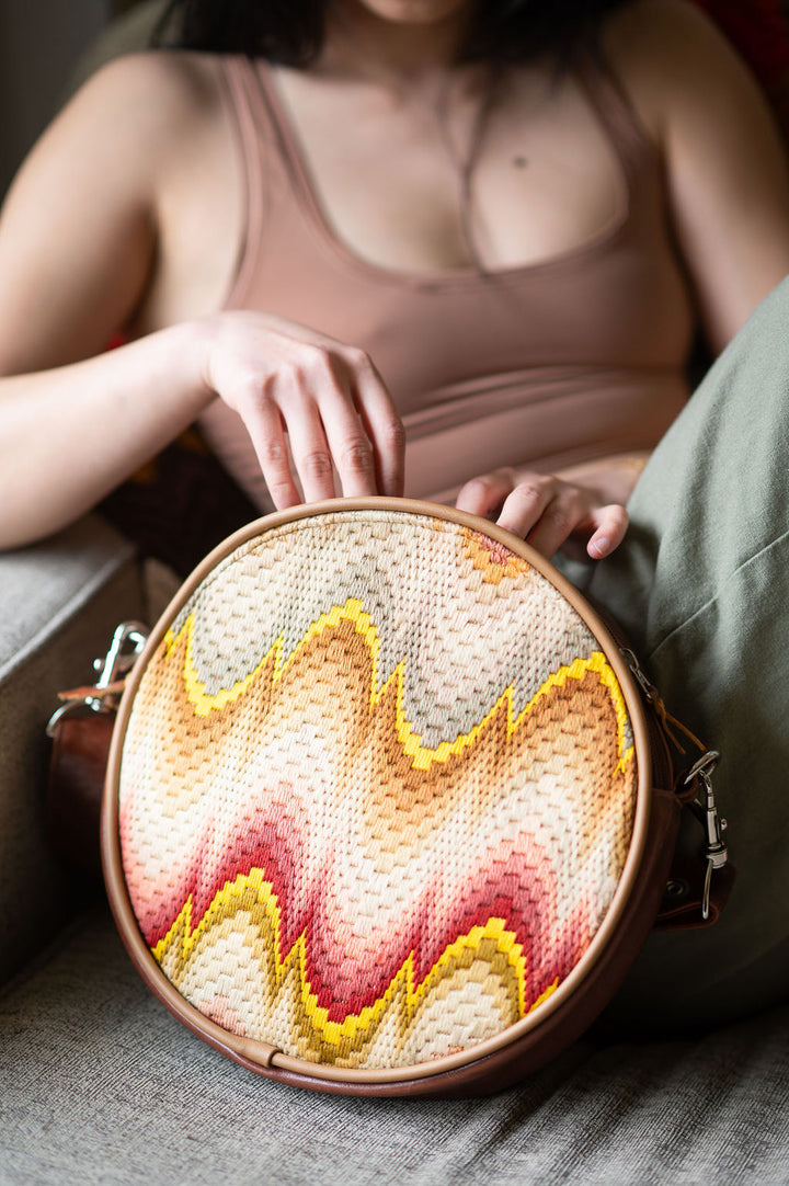 Round woven bag with a wavy pattern held by a person wearing a pink dress#color_bargello-needlepoint