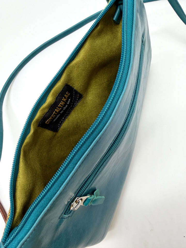 Close-up of a teal handbag with a visible brand label on a white #color_western-sky-arches-teal-green