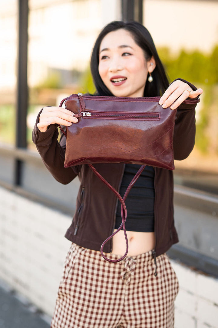Woman holding a brown leather clutch bag outdoors#color_wine