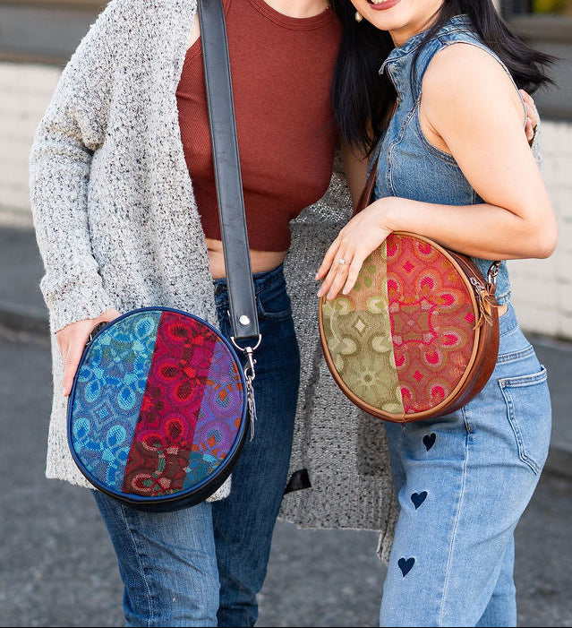 Two people holding colorful round bags in front of a building with large windows.