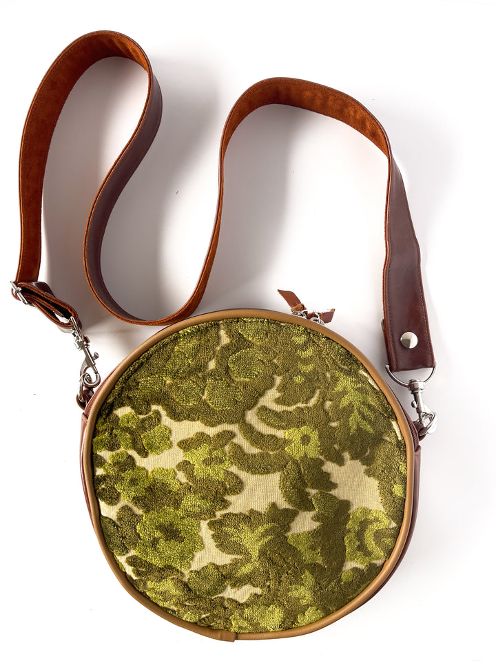 Round bag with green floral pattern and brown strap on a white #color_ornate-mossy-green-chenillebackground