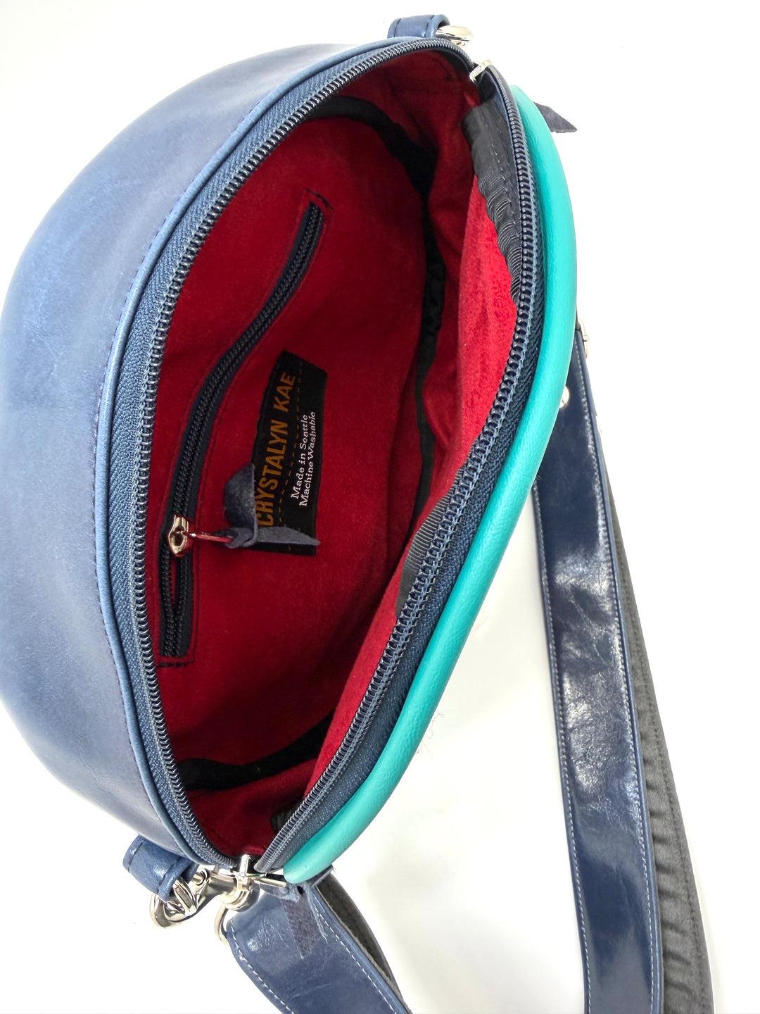 Blue handbag with red interior and visible brand label on a white backgroundRound handbag with colorful abstract pattern on a white background#color_palm-fronds-cool