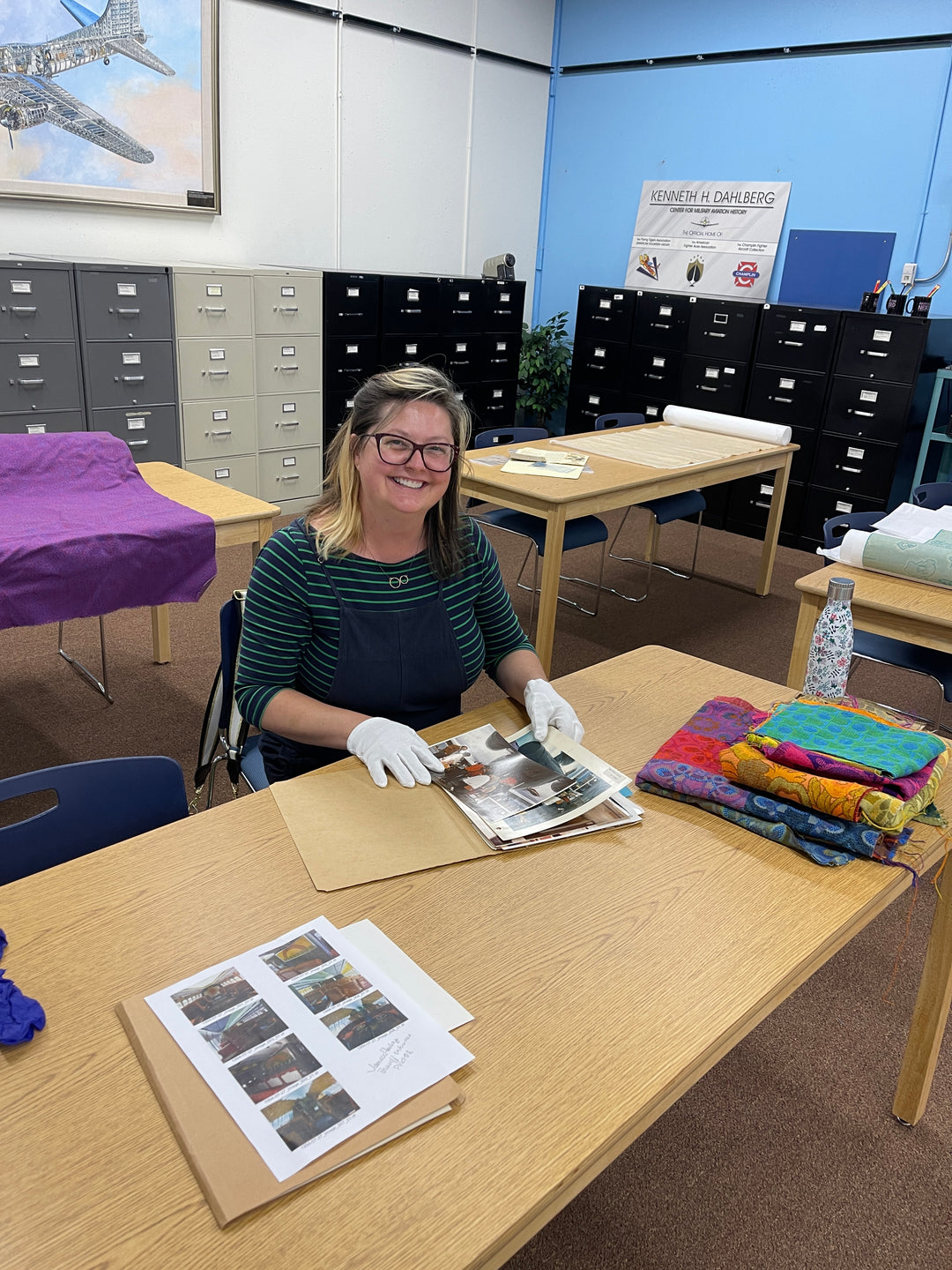 designer crystalyn kae at the museum of flight wearing white gloves looking at archival photos of airplanes interiros from the 1960s