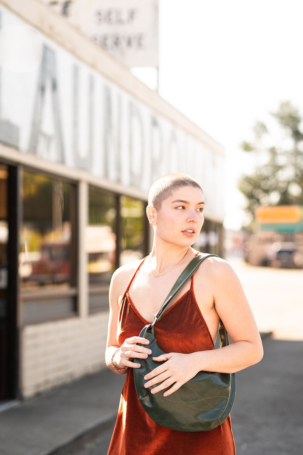Woman in a red dress holding a green bag outdoors with a blurred background#color_emerald-green