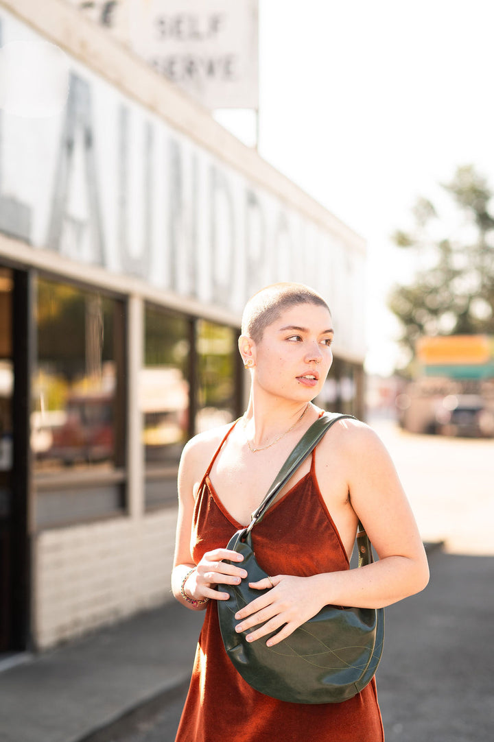 Woman in a red dress holding a green bag outdoors with a blurred background#color_emerald-green