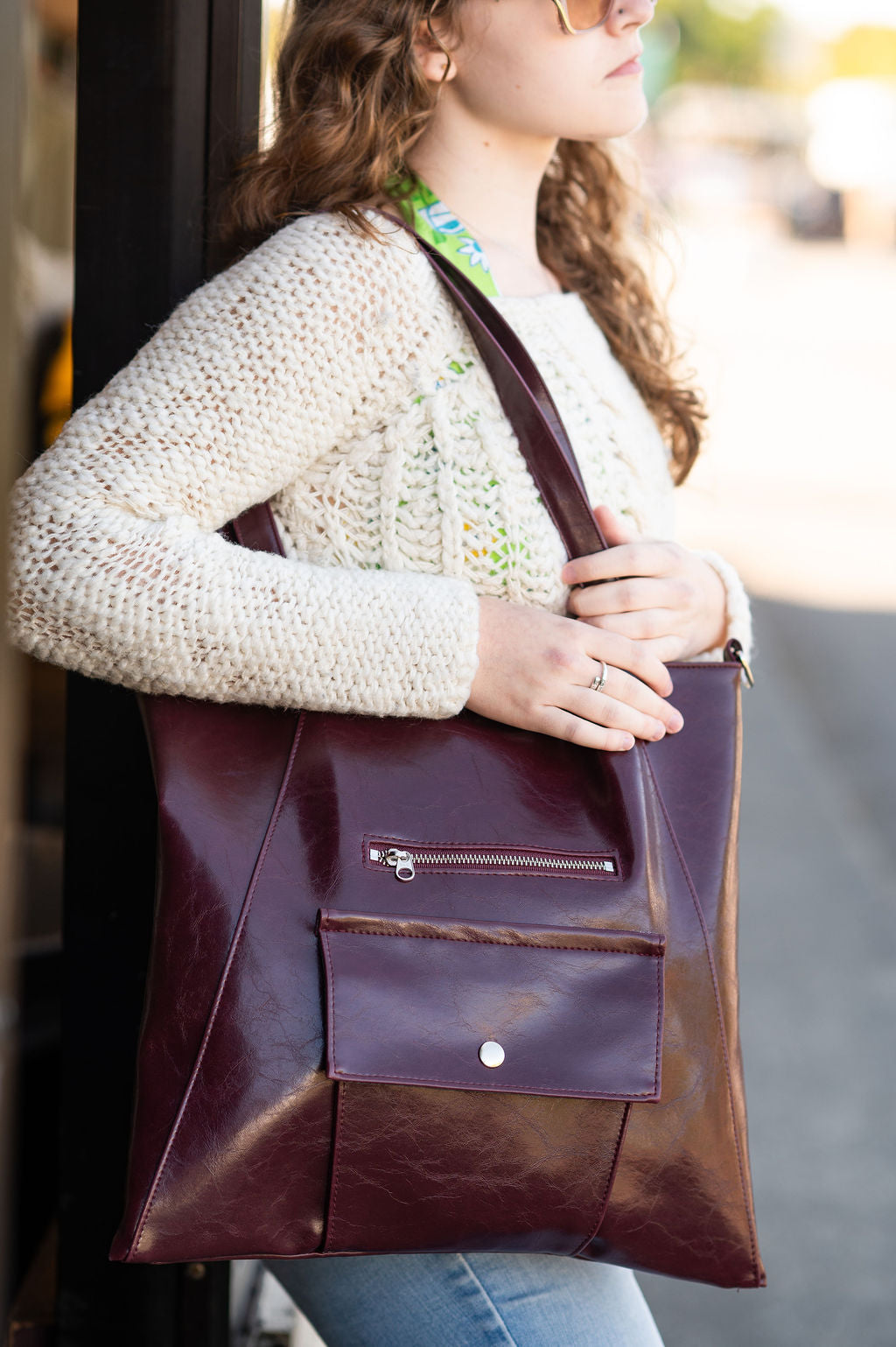 Person holding a brown leather tote bag outdoors#color_wine