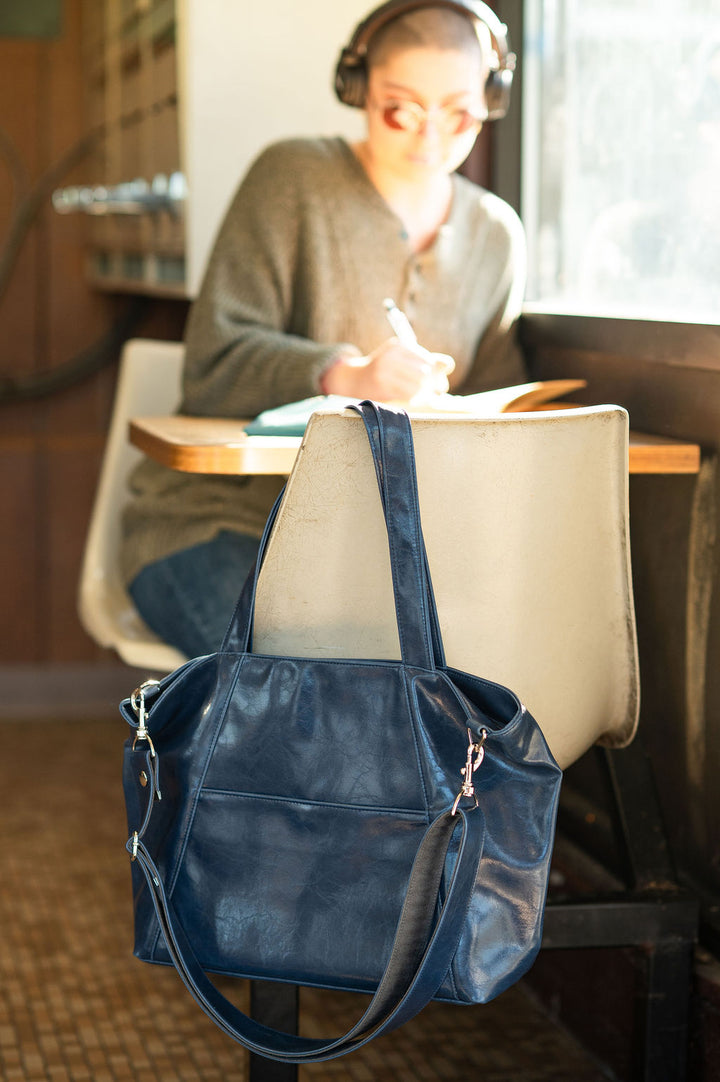 Blue handbag on a chair with a person studying in the background#color_navy