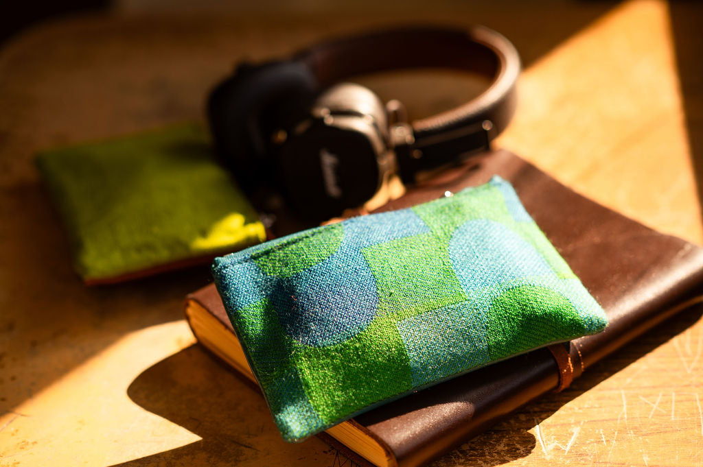Green and blue patterned pouch on a wooden surface with headphones in the background#color_sky-arches-teal-green