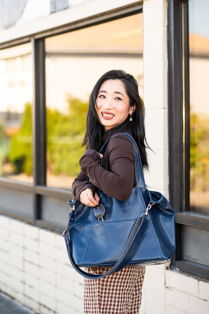 Woman holding a blue laptopt tote handbag in front of a window#color_navy