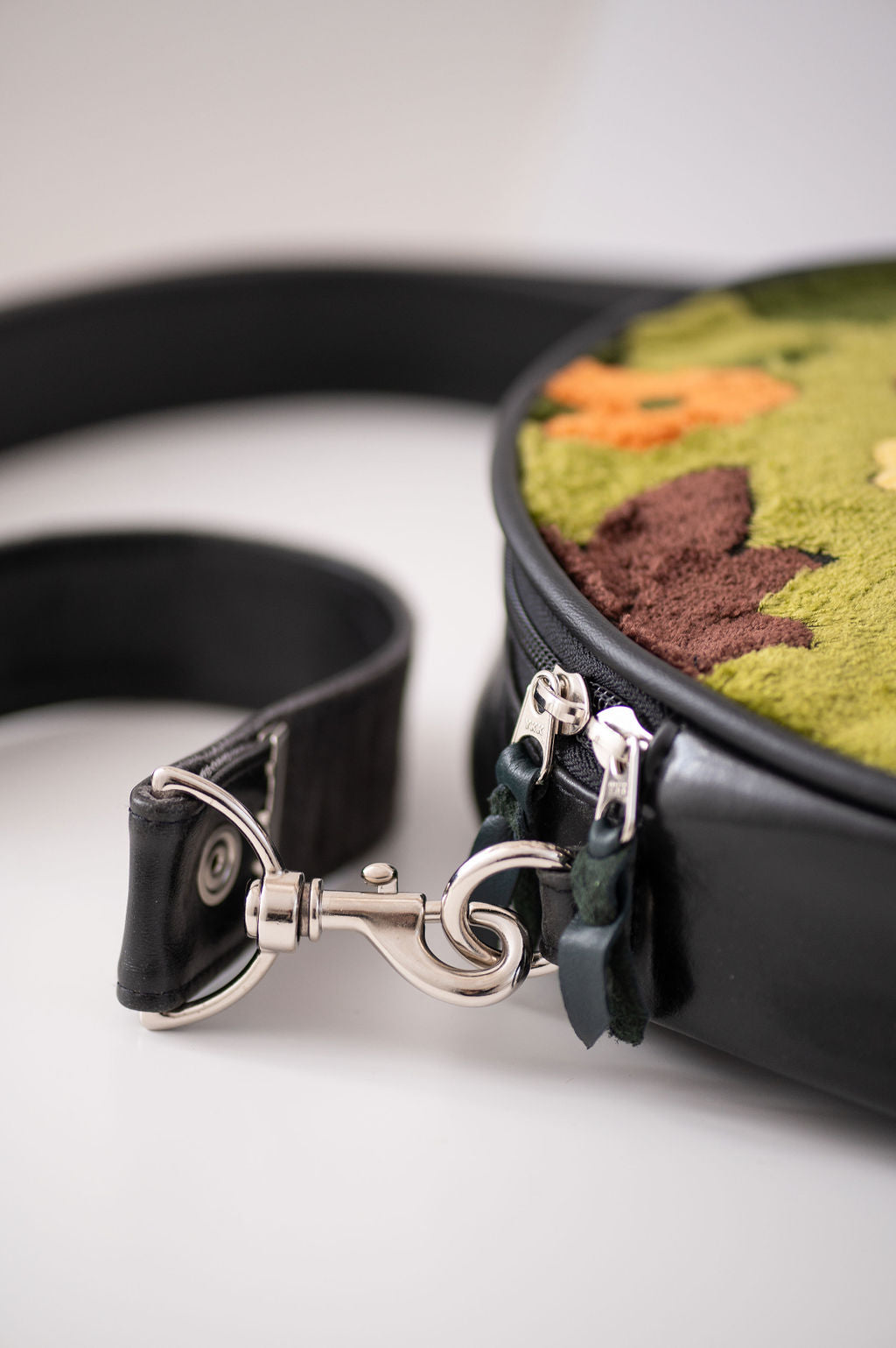 Close-up of a black leather bag with a decorative clasp on a white background#color_groovy-green-floral-chenille