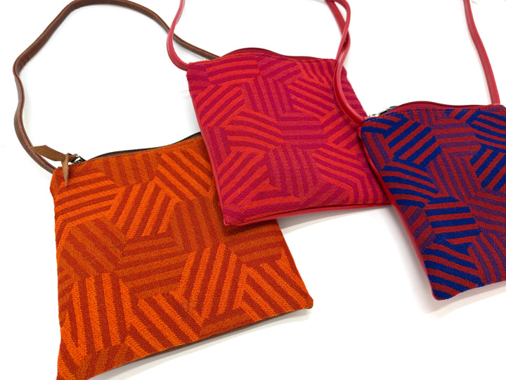 Three hexagon-patterned crossbody bags in red, orange, and blue on a white background#color_hexagon-warm