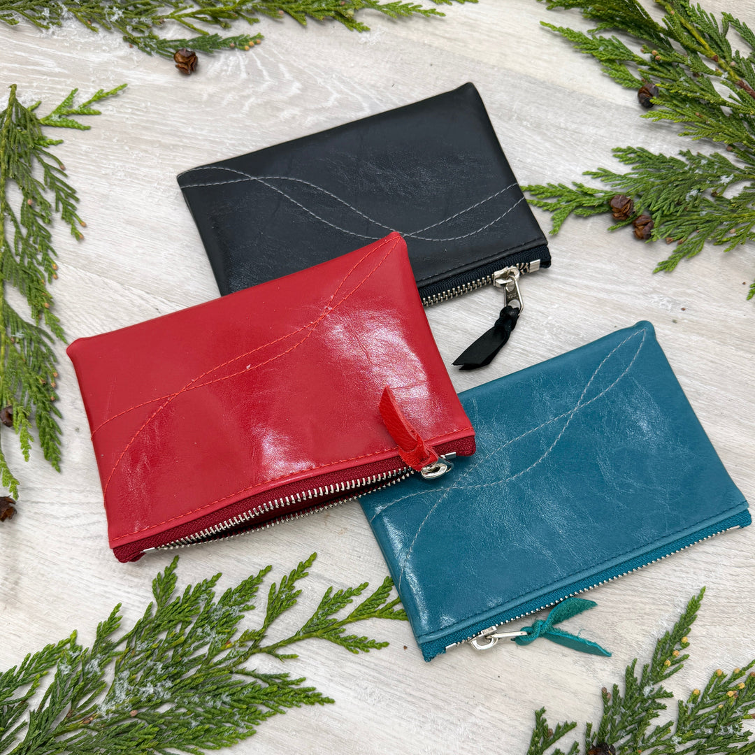 Three leather pouches in black, red, and blue on a white surface with green leaves.