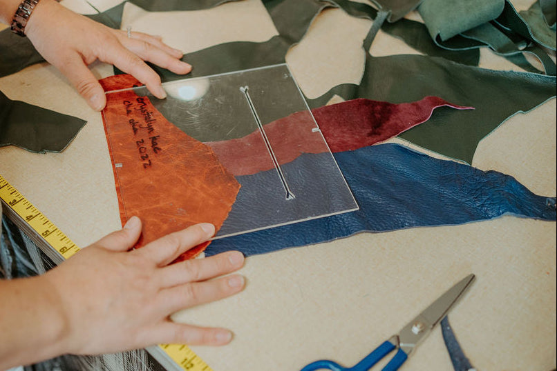 Person cutting leather with a ruler and scissors on a table for patchwork
