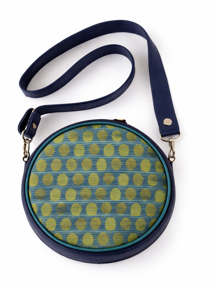 Round crossbody bag with green and blue polka dot pattern on a white background#color_arcade-dots-blue-green