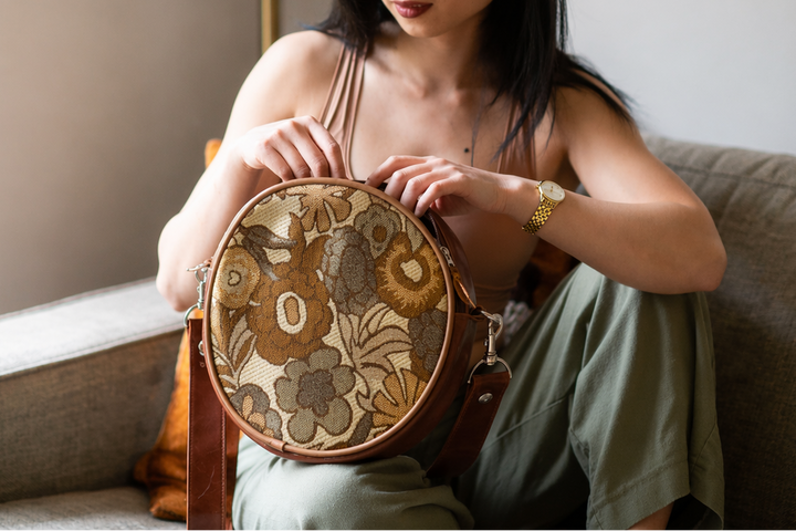 Woman holding a round, embroidered bag in a cozy indoor setting#color_sunset-bloom