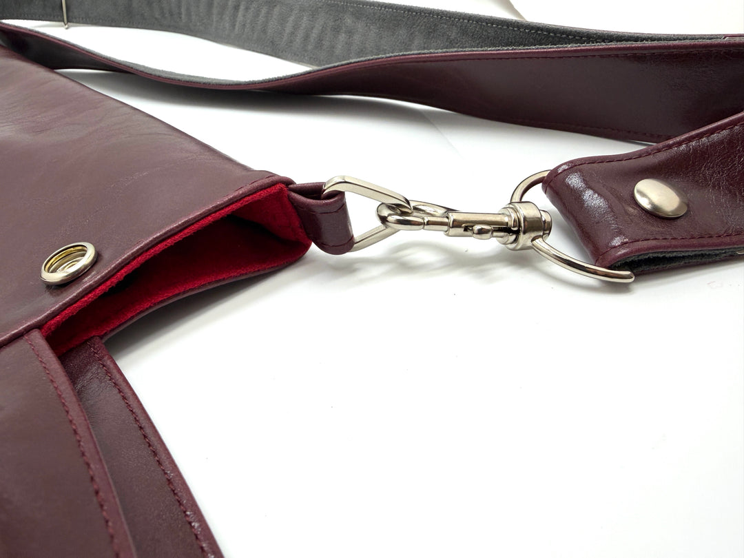 Close-up of a burgundy leather bag with a strap on a white background#color_wine
