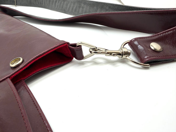 Close-up of a burgundy leather bag with a strap on a white background#color_wine
