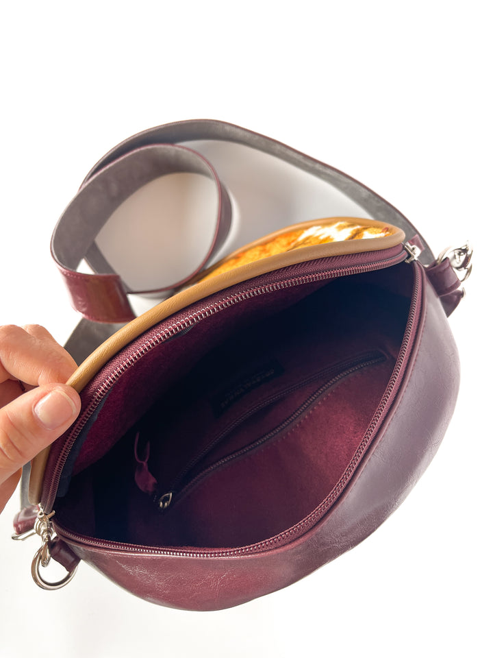 Hand holding a maroon handbag open to reveal its interior.#color_golden-floral-chenille